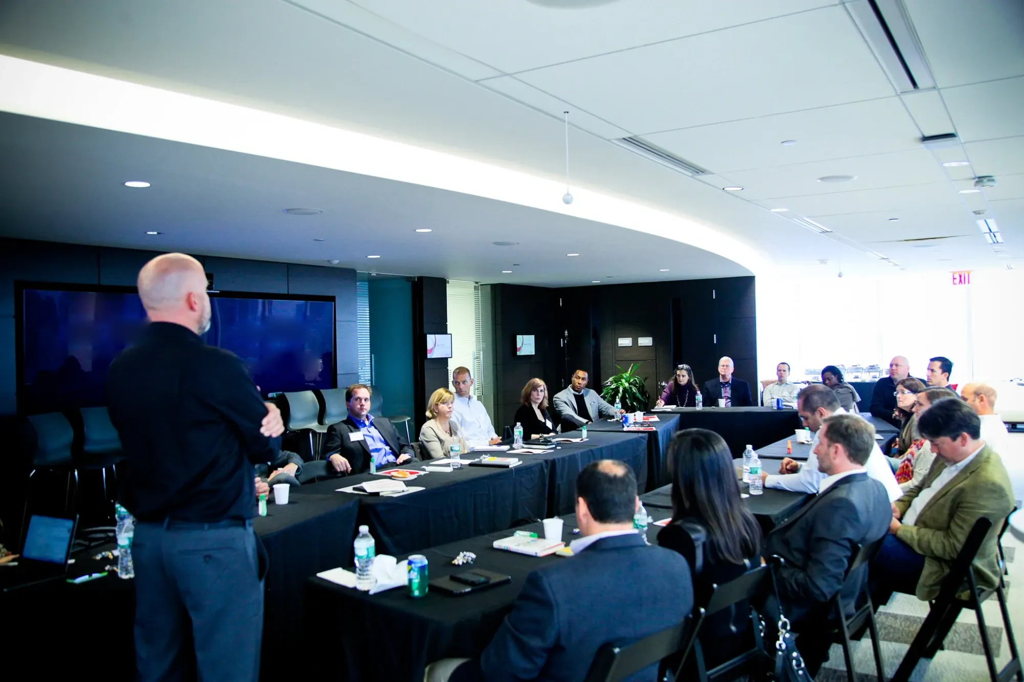 Angus Nelson facilitating a leadership session at the front of a U-shaped table of executives